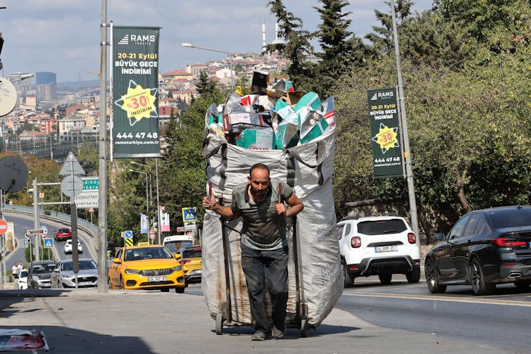 A waste picker hauling a huge bag of plastic waste down a busy street in Istanbul.