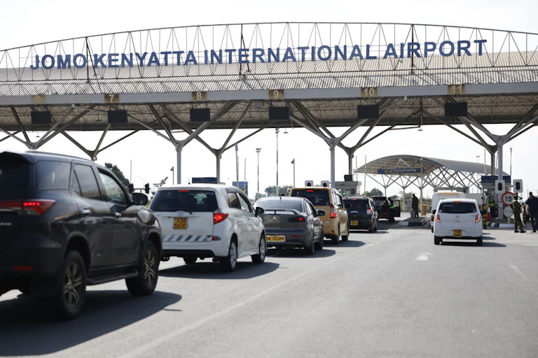 Line of cars approaching an overhead structure with signage saying Jomo Kenyatta International Airport