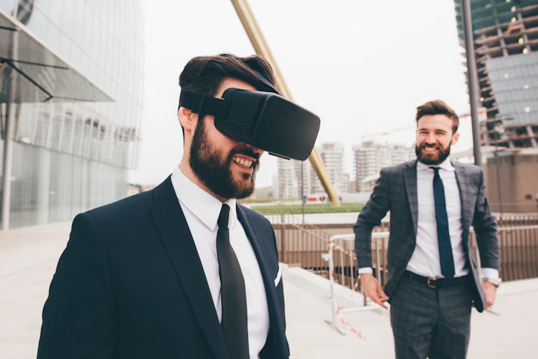 Un homme en costume porte un casque de réalité virtuelle et sourit. Un autre homme le regarde en souriant.
