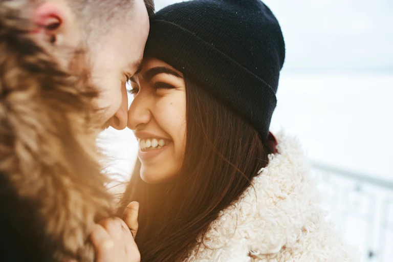 Woman in warm hat rubbing noses with man in coat