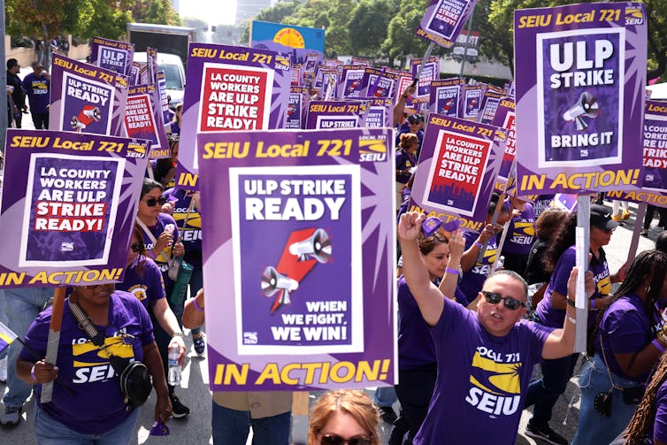 People in purple t-shirts hold signs saying they are ready to hold a strike.