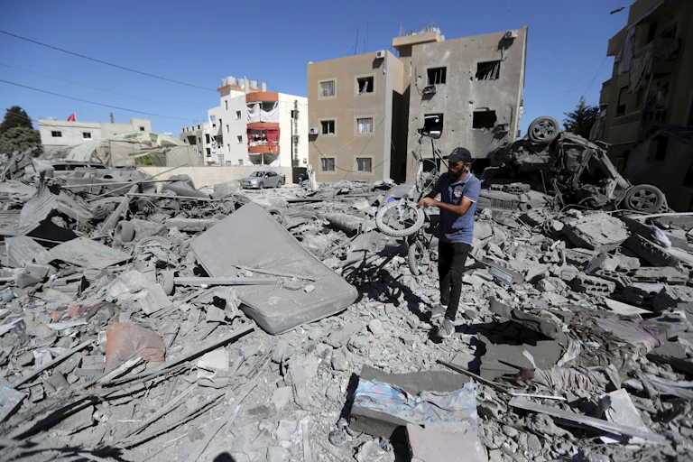 A man holds a wheel amid ash and rubble