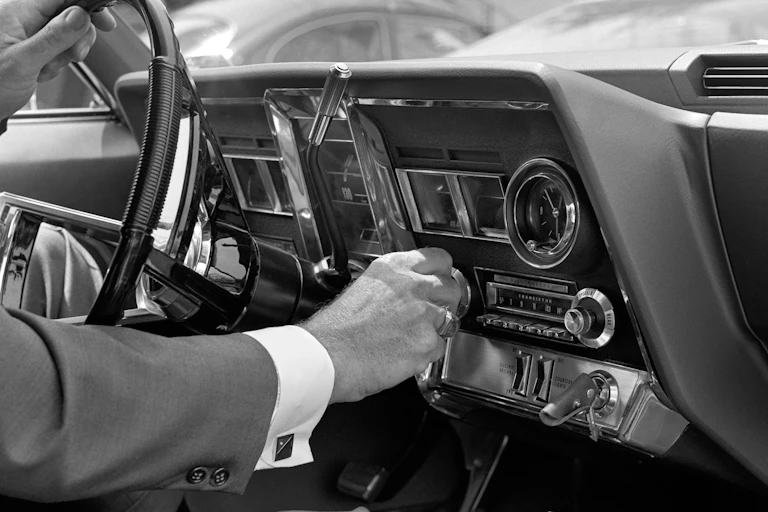 Black and white photo of a hand adjusting the knob of a car radio.