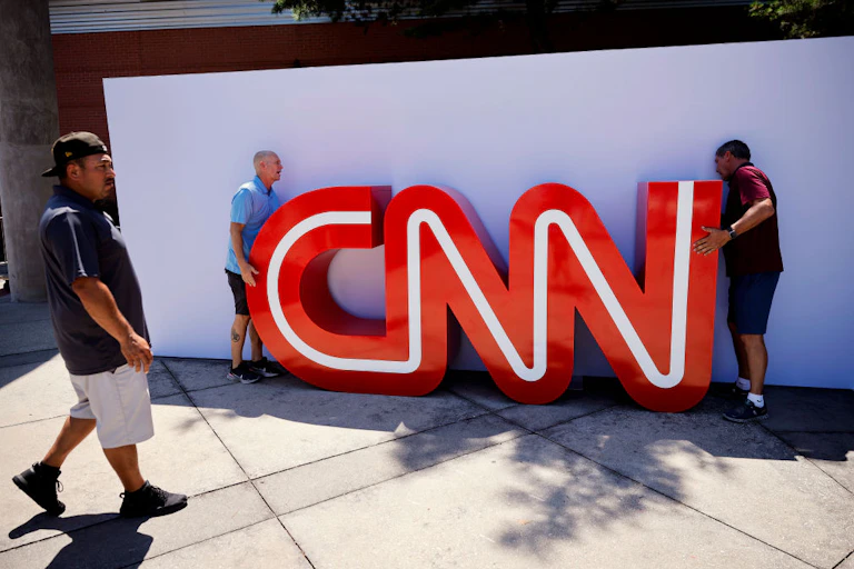 Two men putting a large CNN sign against an outside wall.