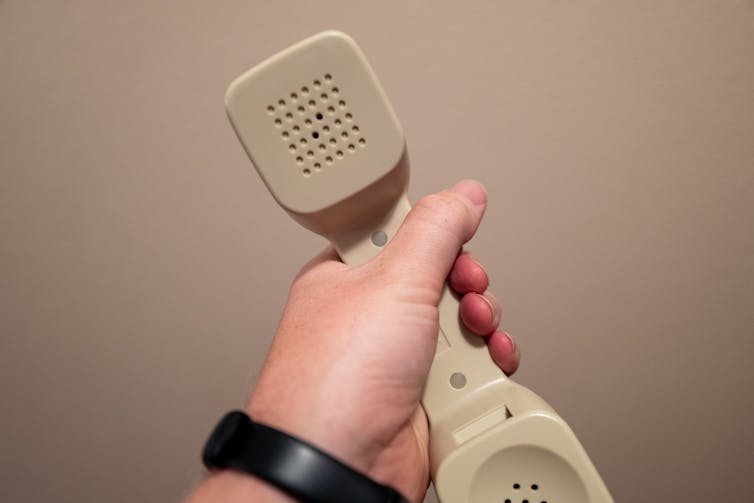 A person's hand holding the beige headset of a traditional landline telephone.