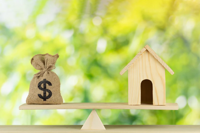 Home and money bag with dollar sign put on the scale
