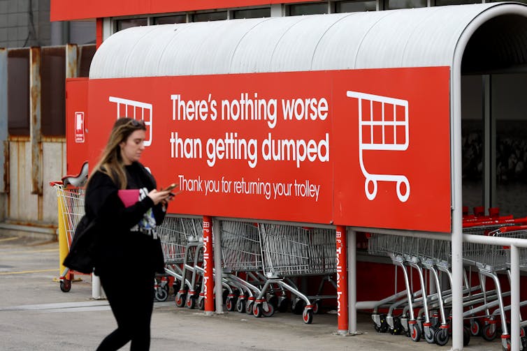 A woman walks past a Coles sign that says there is nothing worse than getting dumped.
