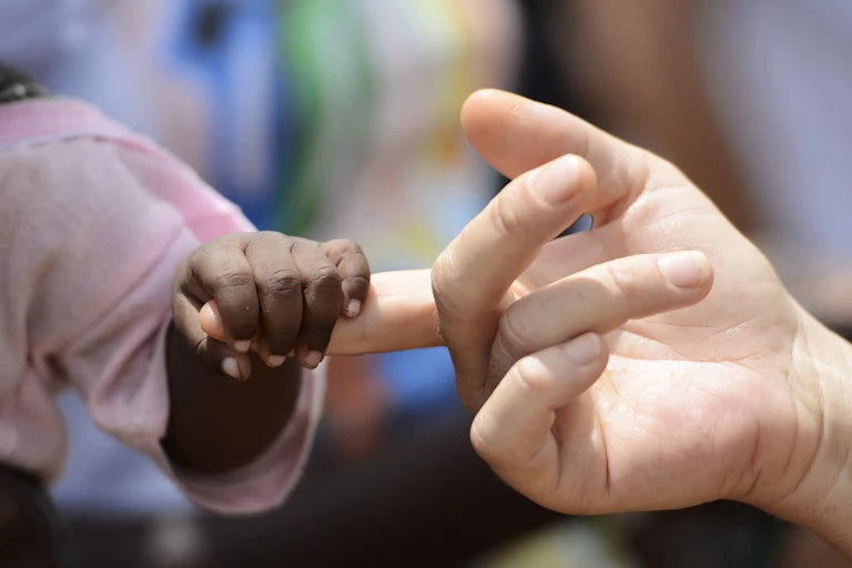 The fingers of a black child curled around one white finger