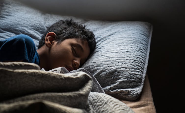 A young boy sleeps in a bed.