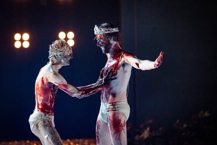 Two men smear blood over each other.