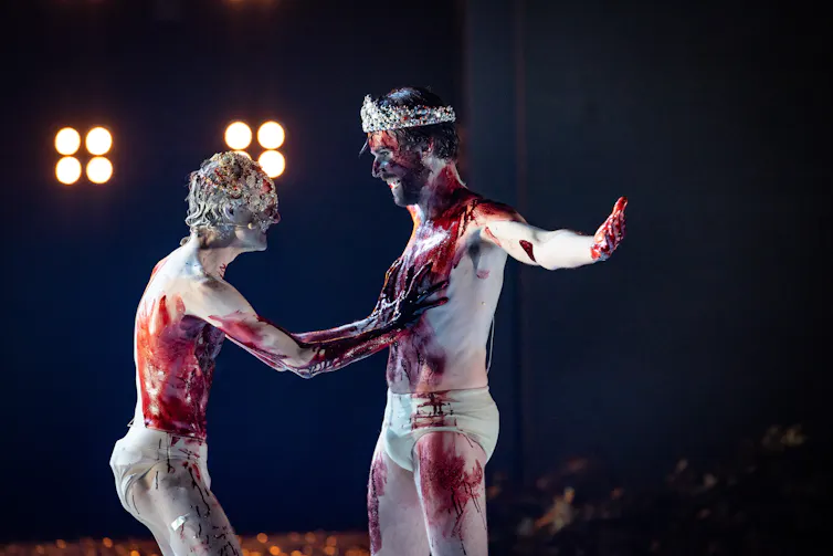 Two men smear blood over each other.