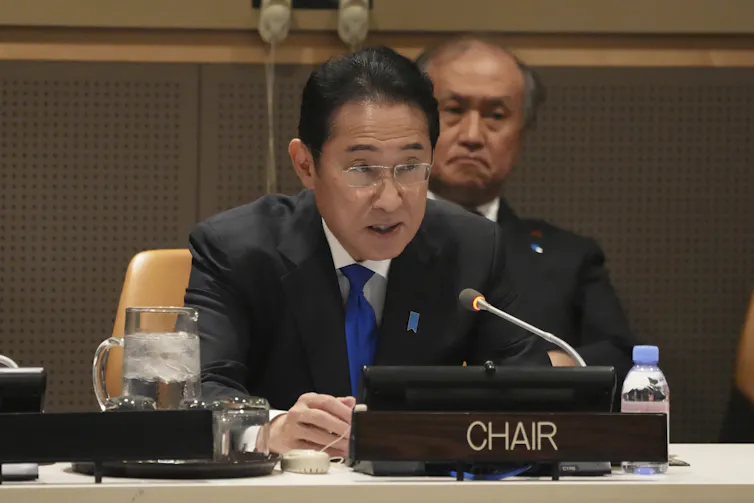 A man in a suit and blue tie speaks into a microphone,