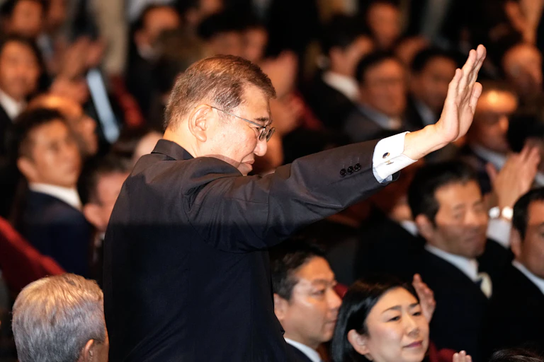 A man in a suit stands and waves at an audience