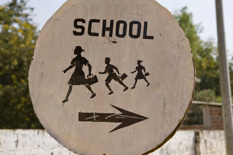 Street sign with the word School, figures of children walking to the left and an arrow pointing right