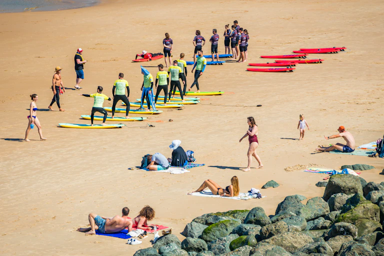 la plage des apprentis surfeurs sur la plage à biarritz apprenent les mouvements de base au milieu de personnes qui bronzent sur la plage simultanément.