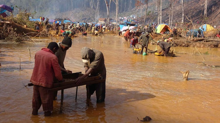 three miners sieving for sapphires, brown river in background