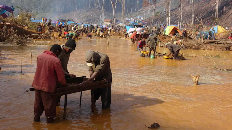 three miners sieving for sapphires, brown river in background