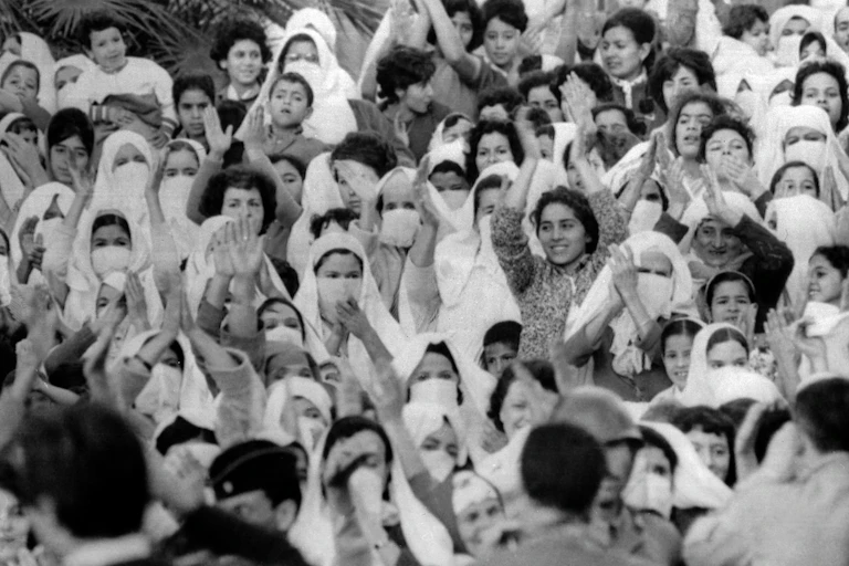 A black and white photo of a crowd of women clapping, smiling and raising their hands.