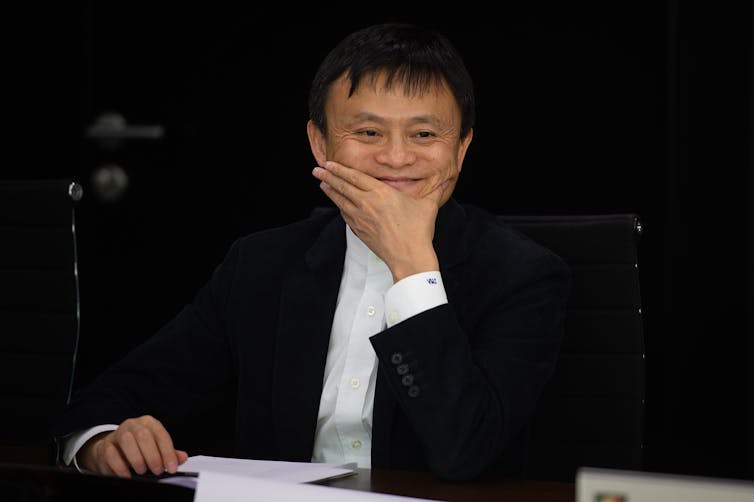 Jack Ma Yun smiling while holding his hand over his face.