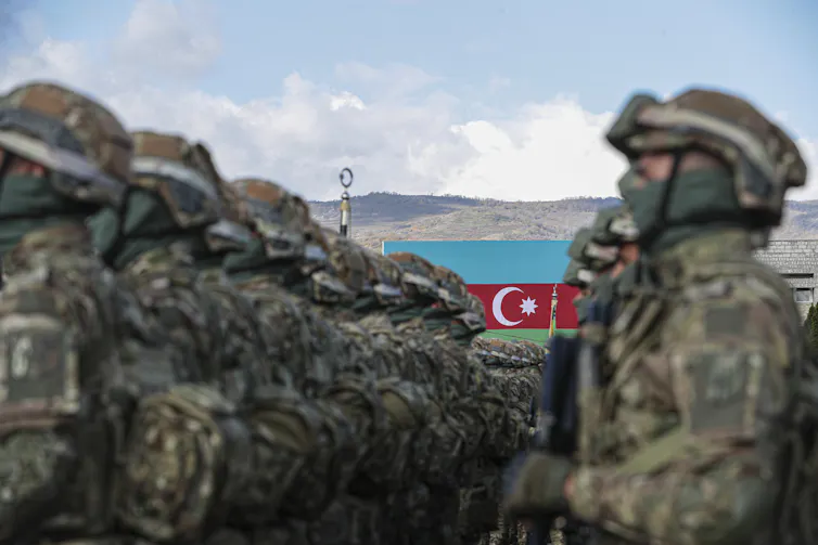Azeri soldiers stood at a parade in front of the Azerbaijan national flag.