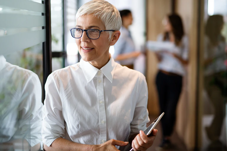 Une femme avec un chemisier blanc des lunettes et des cheveux courts , visiblement elle a tous les atouts de la dirigeante