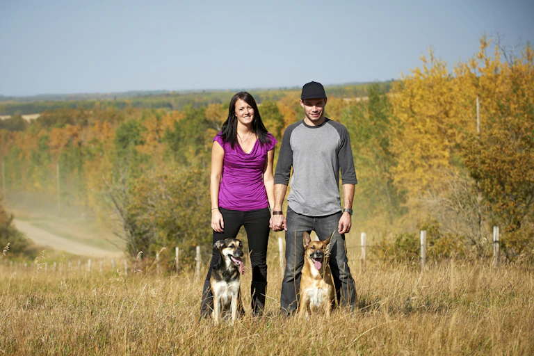 A couple holding hands next to their two dogs in a field.