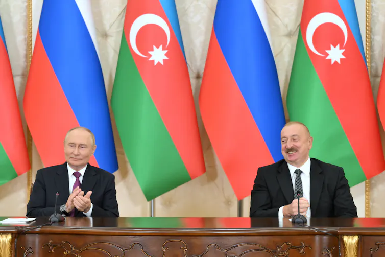 Vladimir Putin and Ilham Aliyev sat next to each other at a desk in front of their respective national flags.