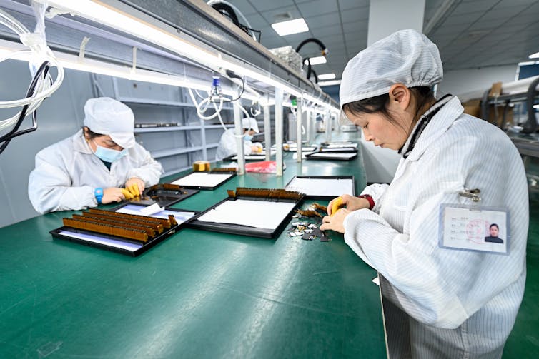 people in white coats and head coverings work on a Chinese semiconductor assembly line