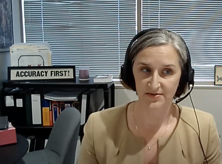 A woman wearing headphones and a microphone in an office where a sign says, in capital letters, 'ACCURACY FIRST!'