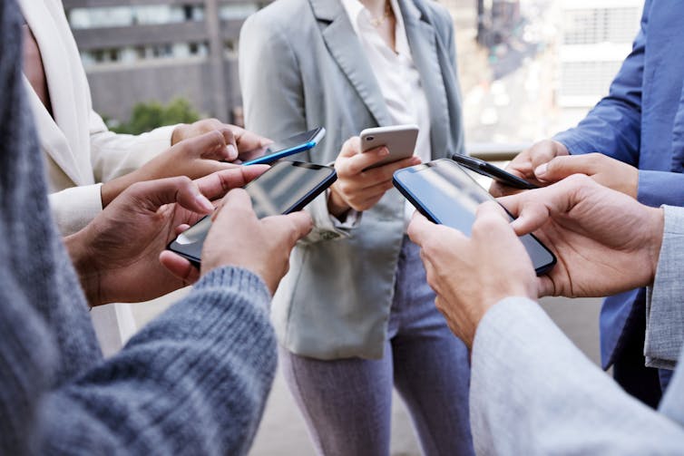 A small group of people in blazers and business attire stand in a circle while using their cell phones