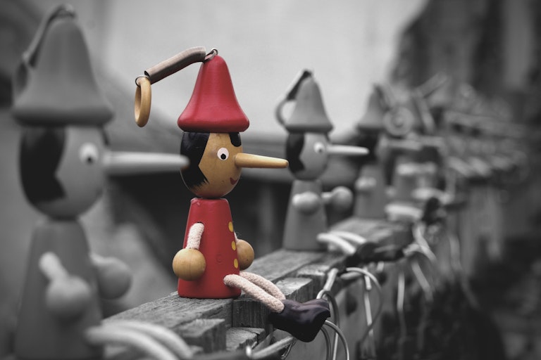 A row of wooden dolls with red hats and elongated noses.