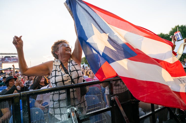 Woman holds up large Puerto Rico flag with crowd behind her