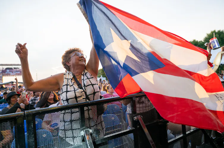Woman holds up large Puerto Rico flag with crowd behind her
