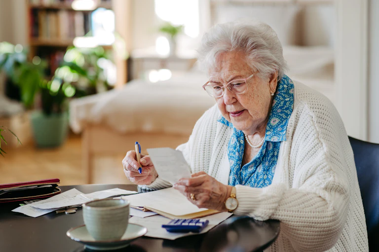 Woman with white hair and glasses looking intently at paperwork with a pen in her hand