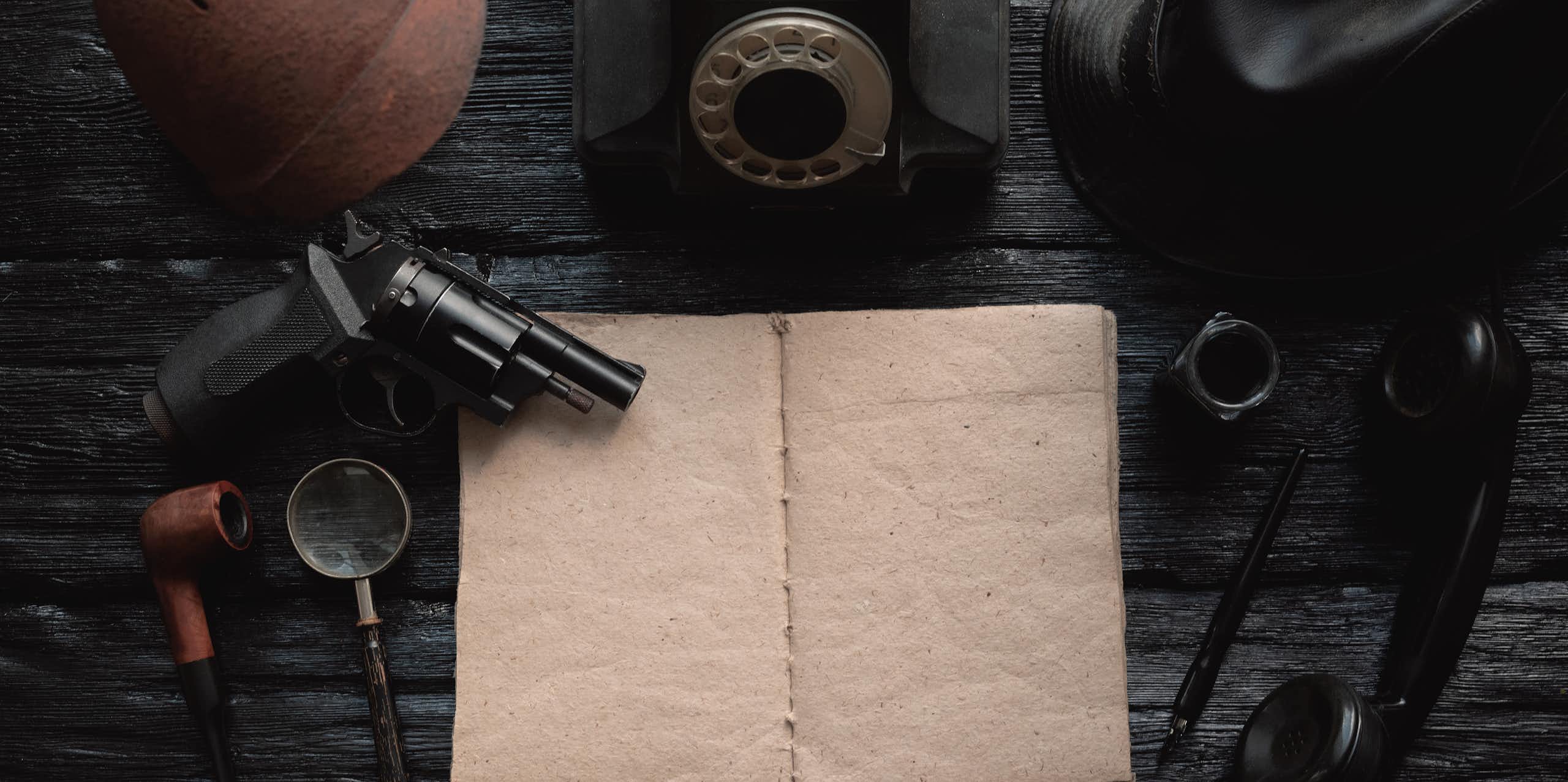 An empty book is surrounded by a gun, a magnifying glass and other tools used by private detectives.