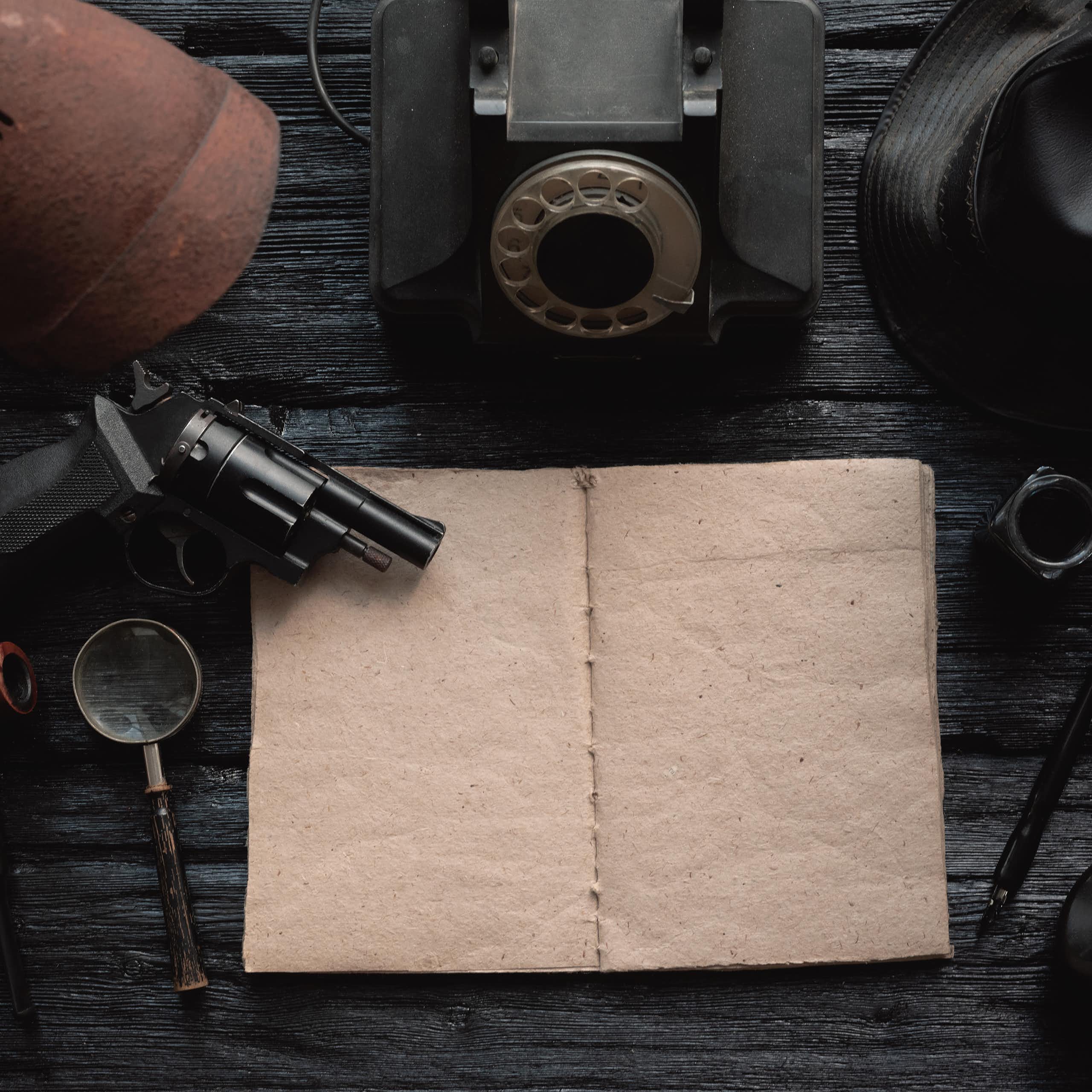 An empty book is surrounded by a gun, a magnifying glass and other tools used by private detectives.