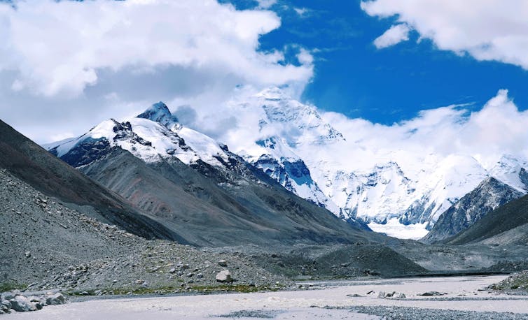 Photo of a riverbed in front of distant snowy mountain peaks.