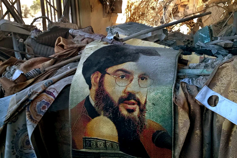 The image of a man in glasses and a beard is seen on a rug amid rubble.