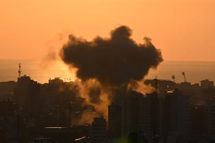 A plume of black smoke is seen rising above buildings.