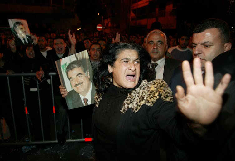 A woman in grief holds her hand out while carrying a photo of a man.
