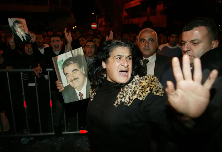 A woman in grief holds her hand out while carrying a photo of a man.