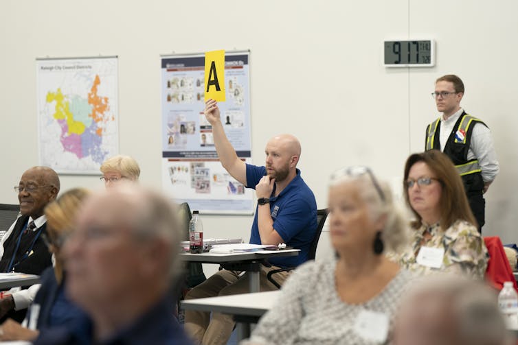 About half a dozen adults at desks in a classroom, looking toward the front.