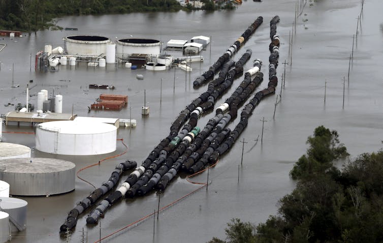 Large storage tanks and dozens of railcars are fully surrounded by floodwater in this aerial view.