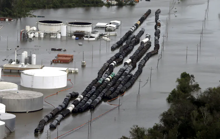Large storage tanks and dozens of railcars are fully surrounded by floodwater in this aerial view.