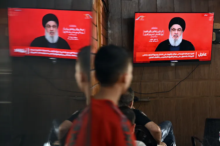 A man watches Hezbollah leader, Hassan Nasrallah, delivering a speech on television screens in a Beirut cafe.