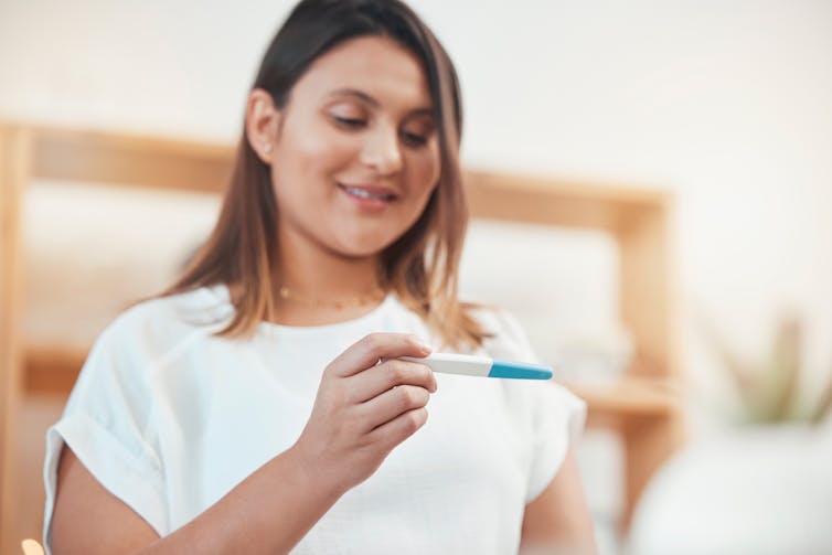 A woman smiles looking at a home pregnancy test.