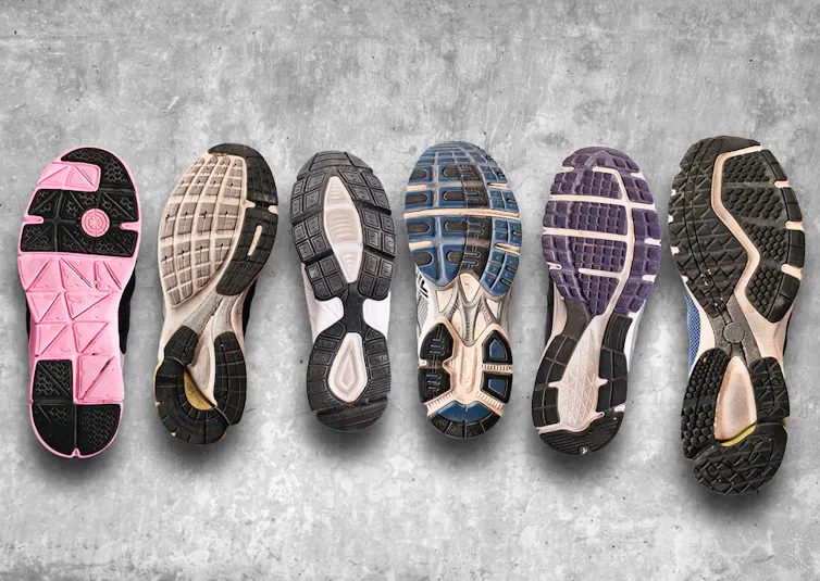A line-up of running shoes on a grey floor with the soles showing various levels of wear.