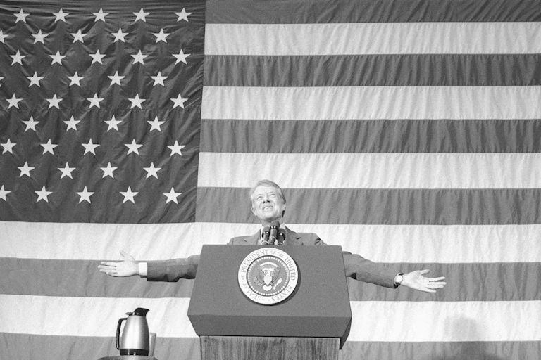 A man stands behind a lectern in front of a giant American flag