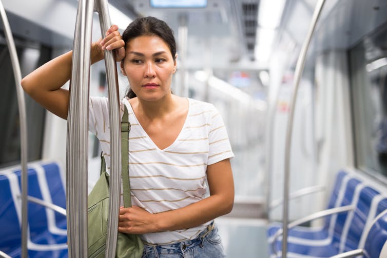 Weary woman leans against a pole in an empty train carriage.