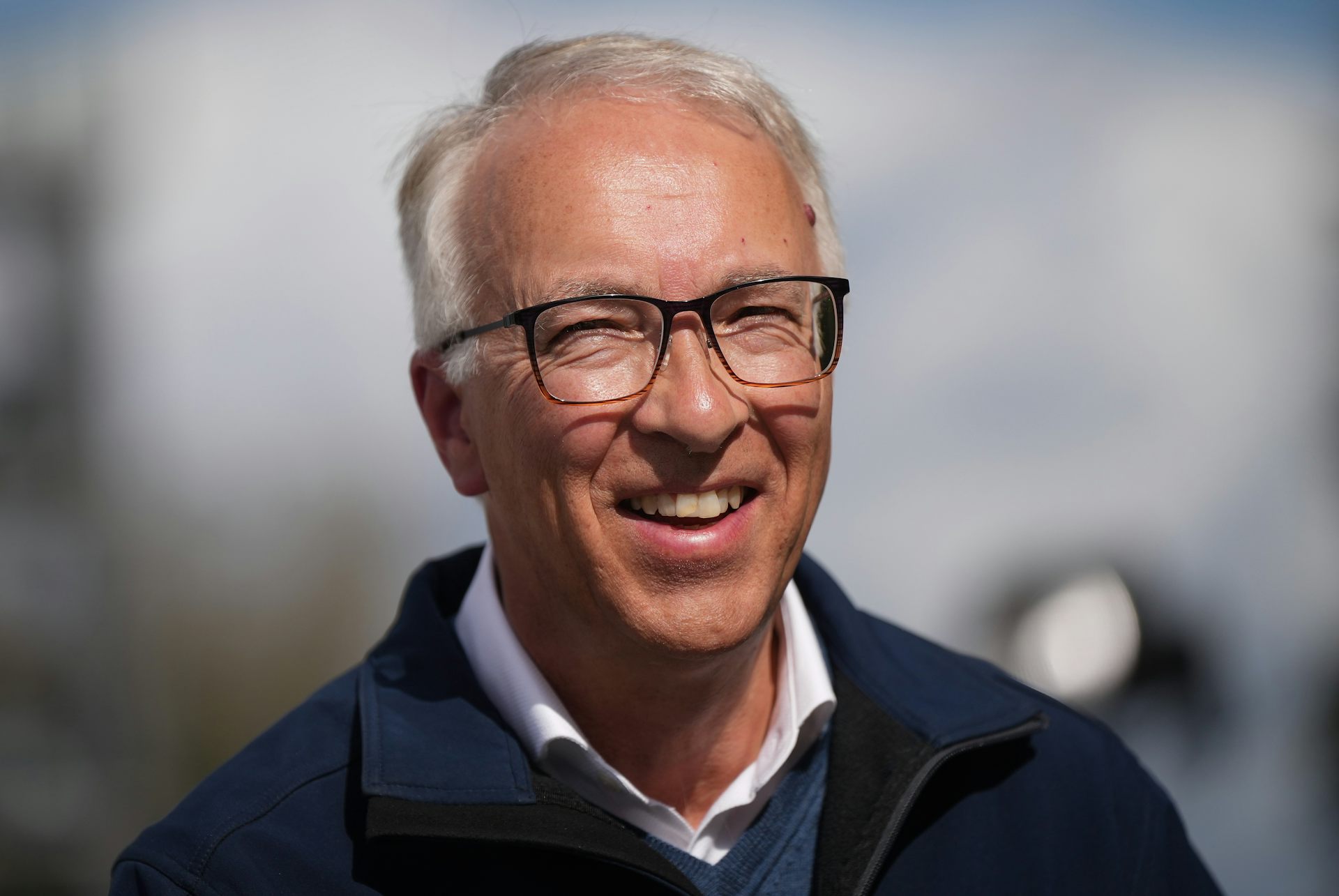 A man with thinning grey hair and wearning glasses smiles.